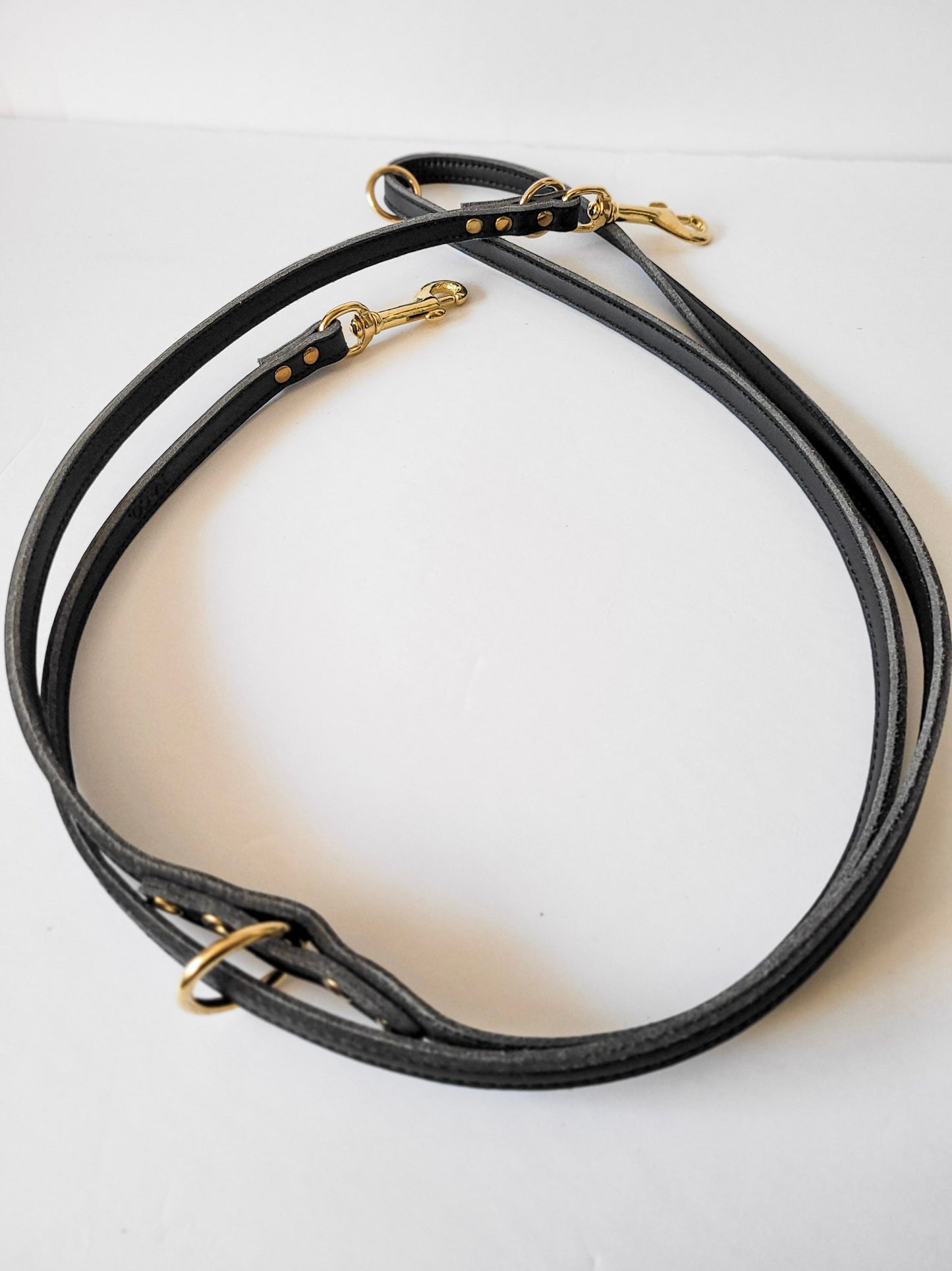 Laisse polyvalente double extrémités avec attaches et anneaux en laiton. Laisse roulé sur fond blanc.