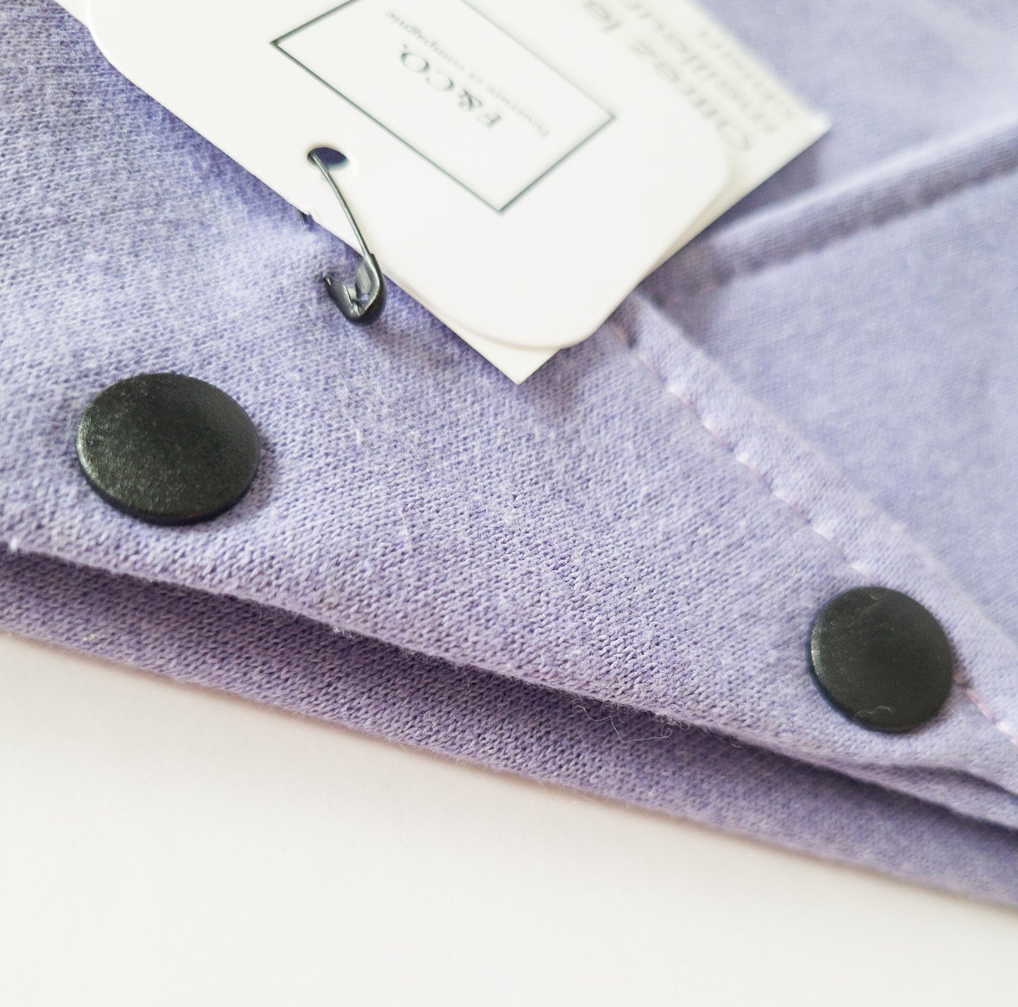 Grosplan sur bouton pression noir mat sur bandanas de coton ouaté violet bleuté.