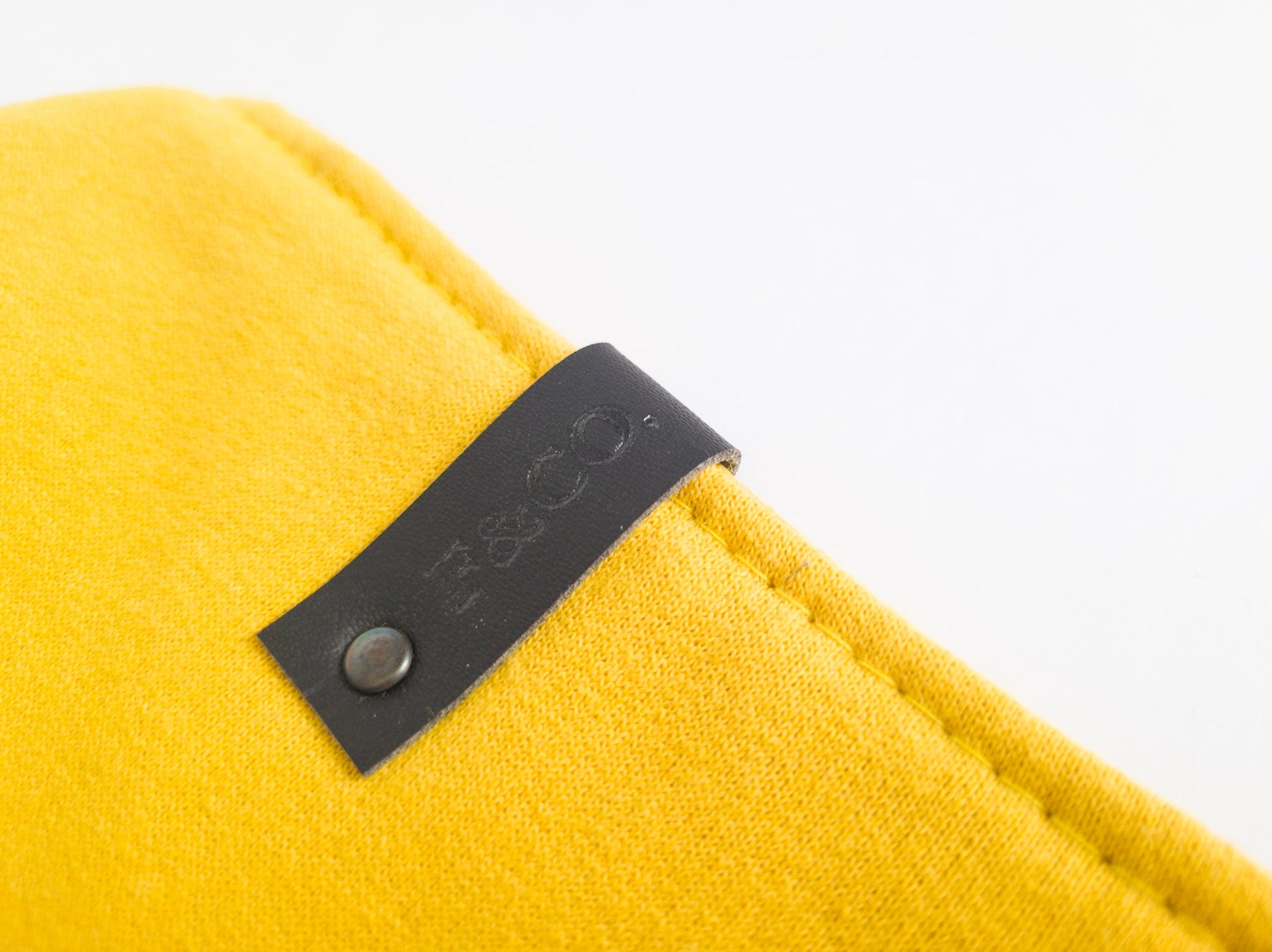 Gros plan sur étiuette de cuir végan noir su bandanas jaune moutarde en coton ouaté.