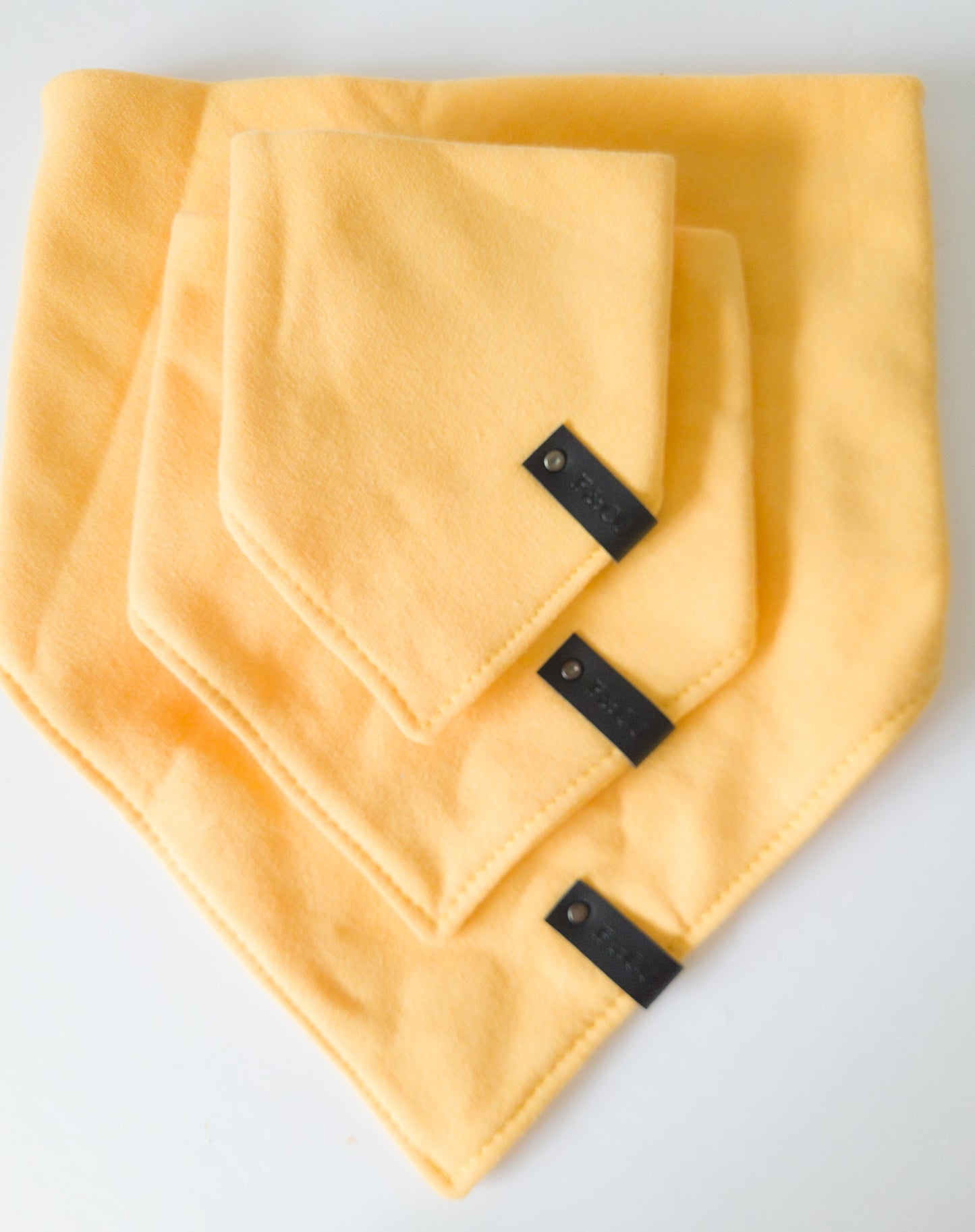 Différentes grandeurs de bandanas de coton ouaté de couleur jaune blé avec étiquettes de cuir végan noir.