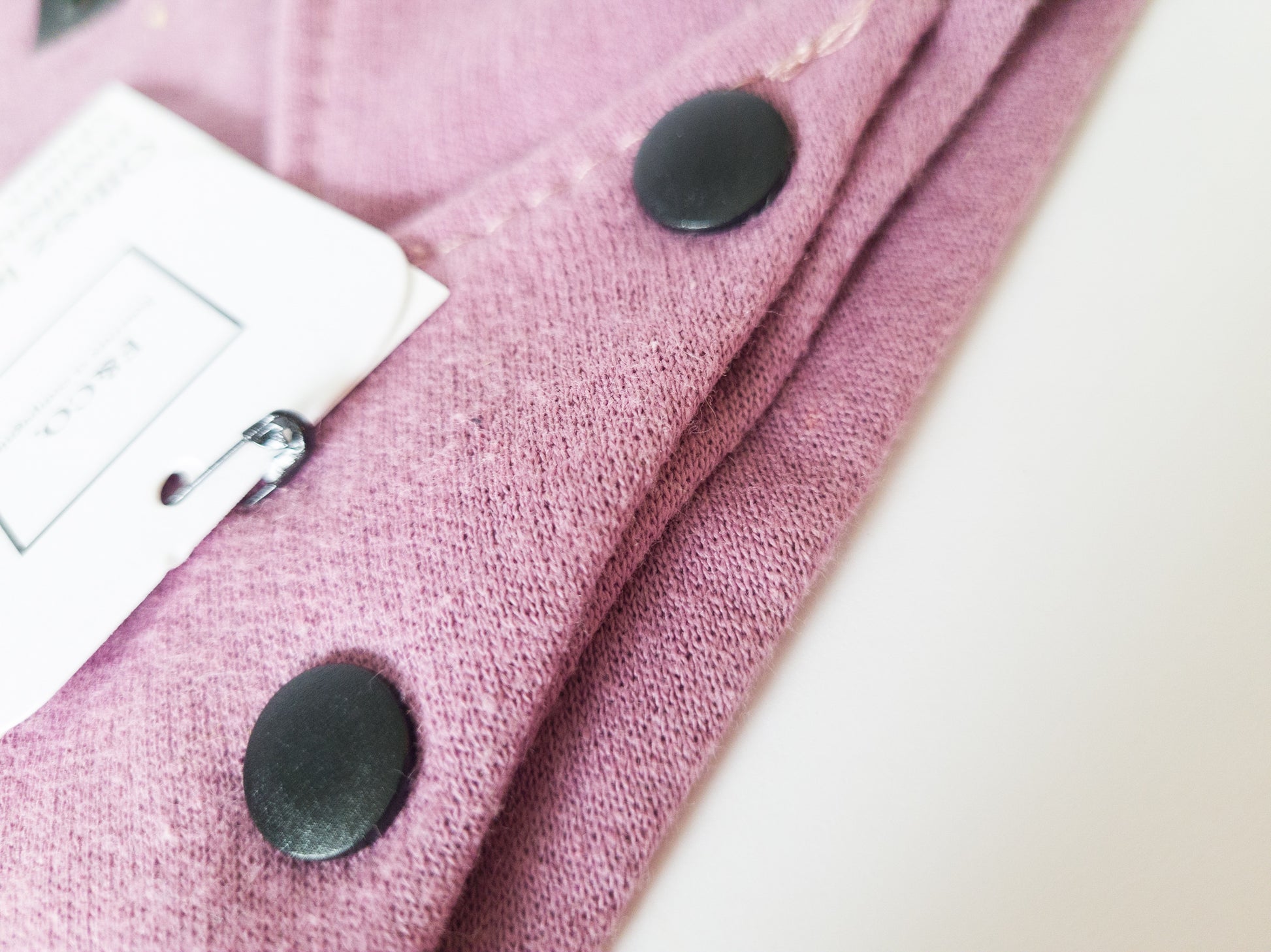 Gros plan sur boutons pression de plastique noir mat sur bandanas violet rosé en coton ouaté.