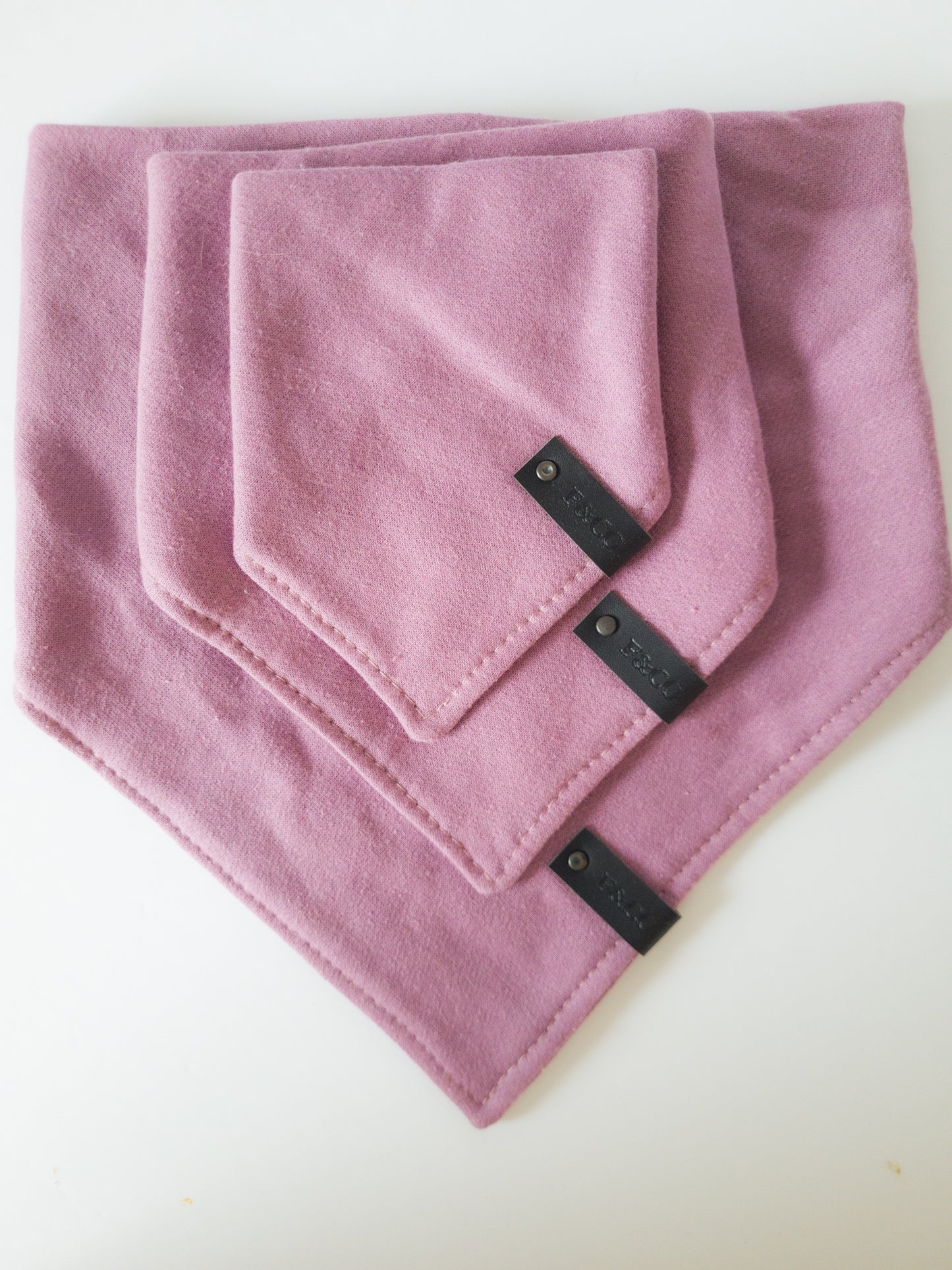 Différentes grandeurs de bandanas de coton ouaté de couleur violet rosé. Étiquettes de cuir noir végan.